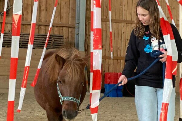 Ein Mädchen führt ein Pony durch herabhängendes Absperrband