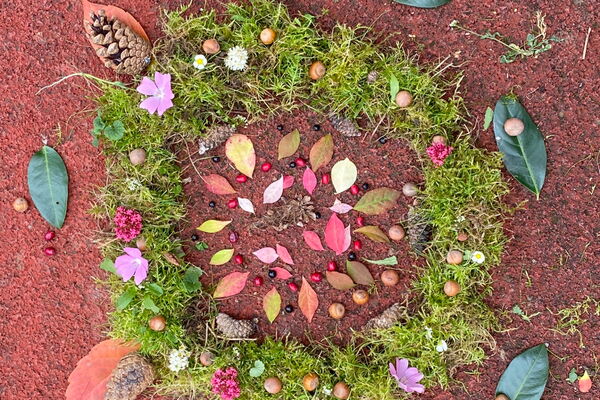 Ein bunter Kranz aus Blättern, Moos und Blüten liegt am Boden