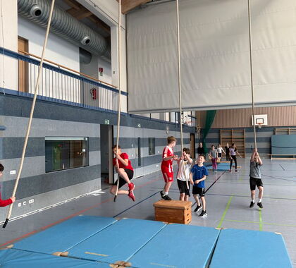Schüler schwingen in der Turnhalle von einem Kasten zum nächsten